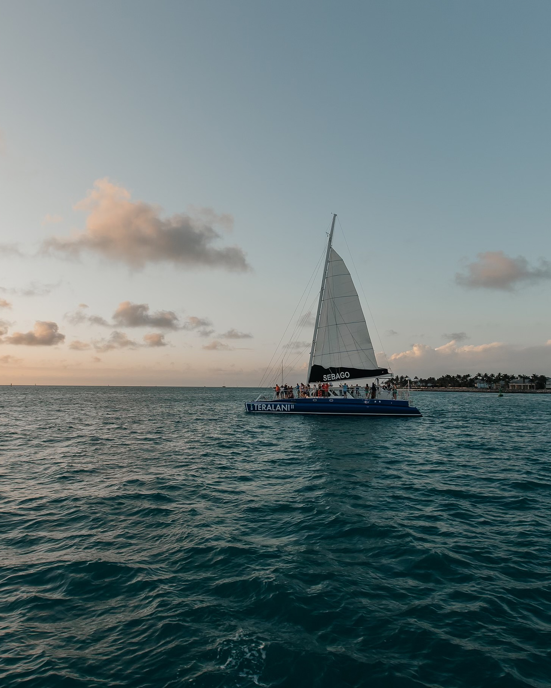 Catamaran sailboat on open water at sunset with passengers on deck
